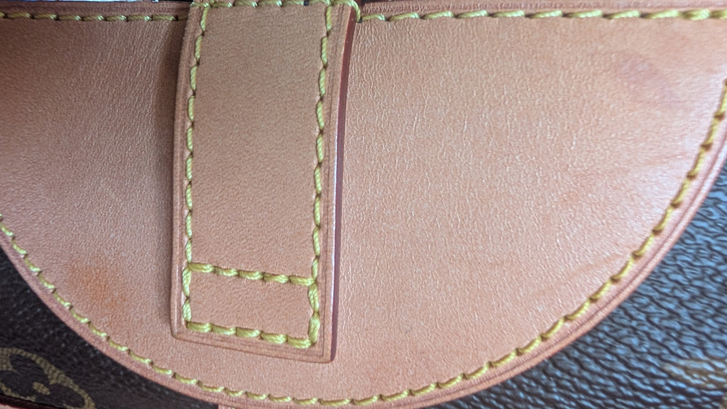 Close-up detail of a light tan leather strap with light green contrast stitching, showing a textured dark brown patterned surface underneath. Pre-Owned Louis Vuitton Duffle Bucket Monogram Canvas - Full Set