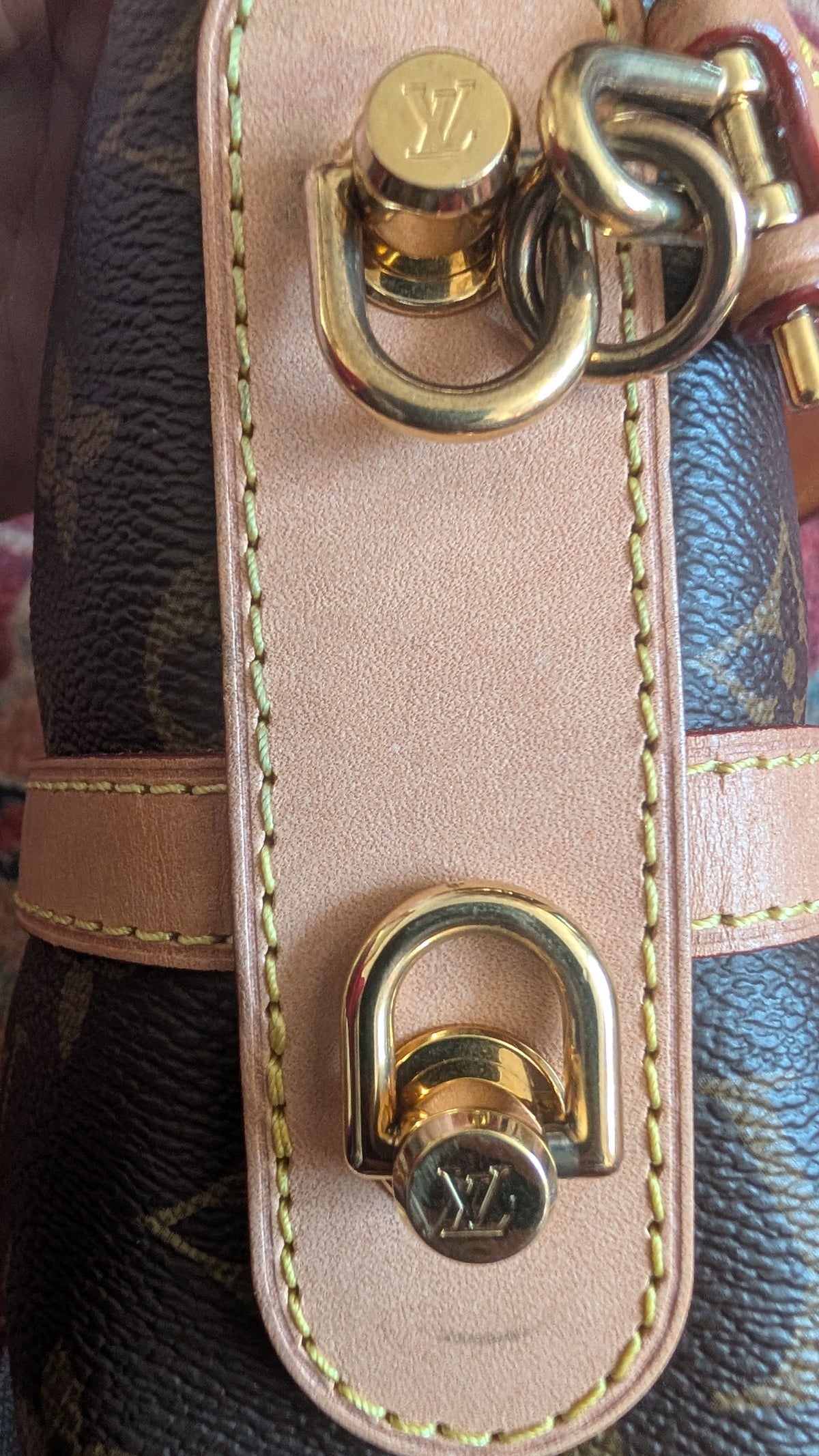 Close-up of a Louis Vuitton handbag showing the signature monogram canvas, a light beige leather strap, and gold-tone hardware with the LV logo engraved on the lock and rings. Pre-Owned Louis Vuitton Duffle Bucket Monogram Canvas - Full Set