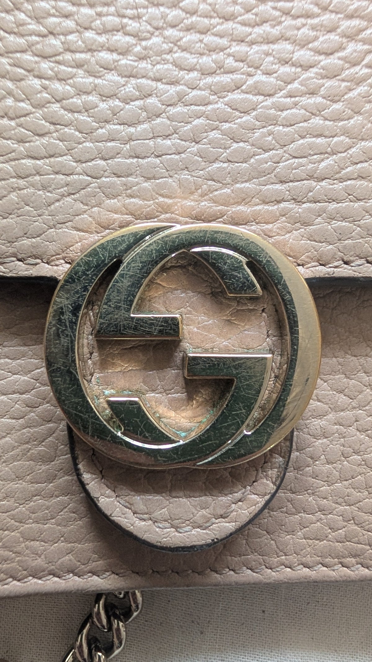 Close-up of a Gucci interlocking GG logo turn-lock closure in gold-tone metal with a green enamel inlay, attached to a light beige pebbled leather strap. Pre-Owned Gucci Interlocking G Chain Wallet / Crossbody – Beige Pebbled Leather