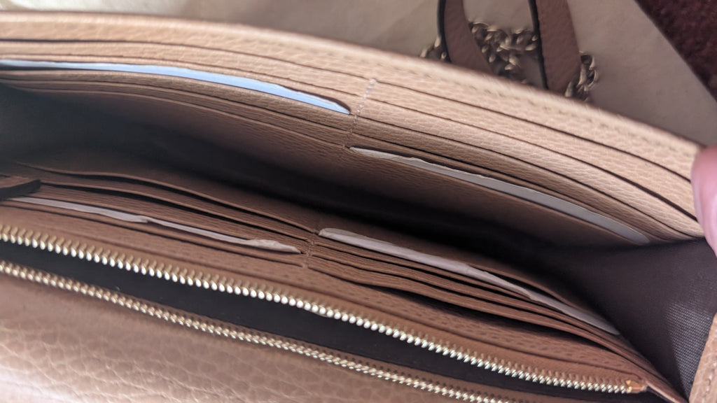 Close-up of the interior of a beige leather wallet or card holder, showing multiple card slots, a zipper, and a dark brown lining, with a hand holding the edge open. Pre-Owned Gucci Interlocking G Chain Wallet / Crossbody – Beige Pebbled Leather