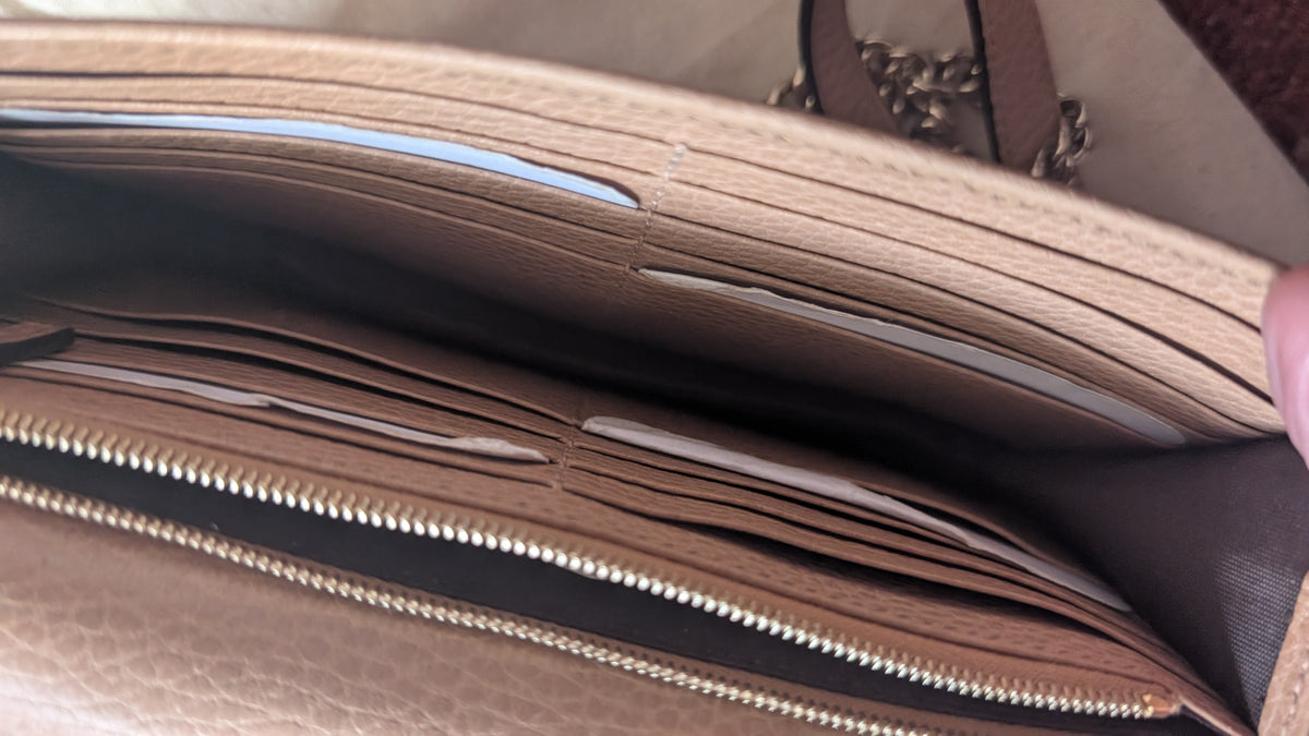Close-up of the interior of a beige leather wallet or card holder, showing multiple card slots, a zipper, and a dark brown lining, with a hand holding the edge open. Pre-Owned Gucci Interlocking G Chain Wallet / Crossbody – Beige Pebbled Leather