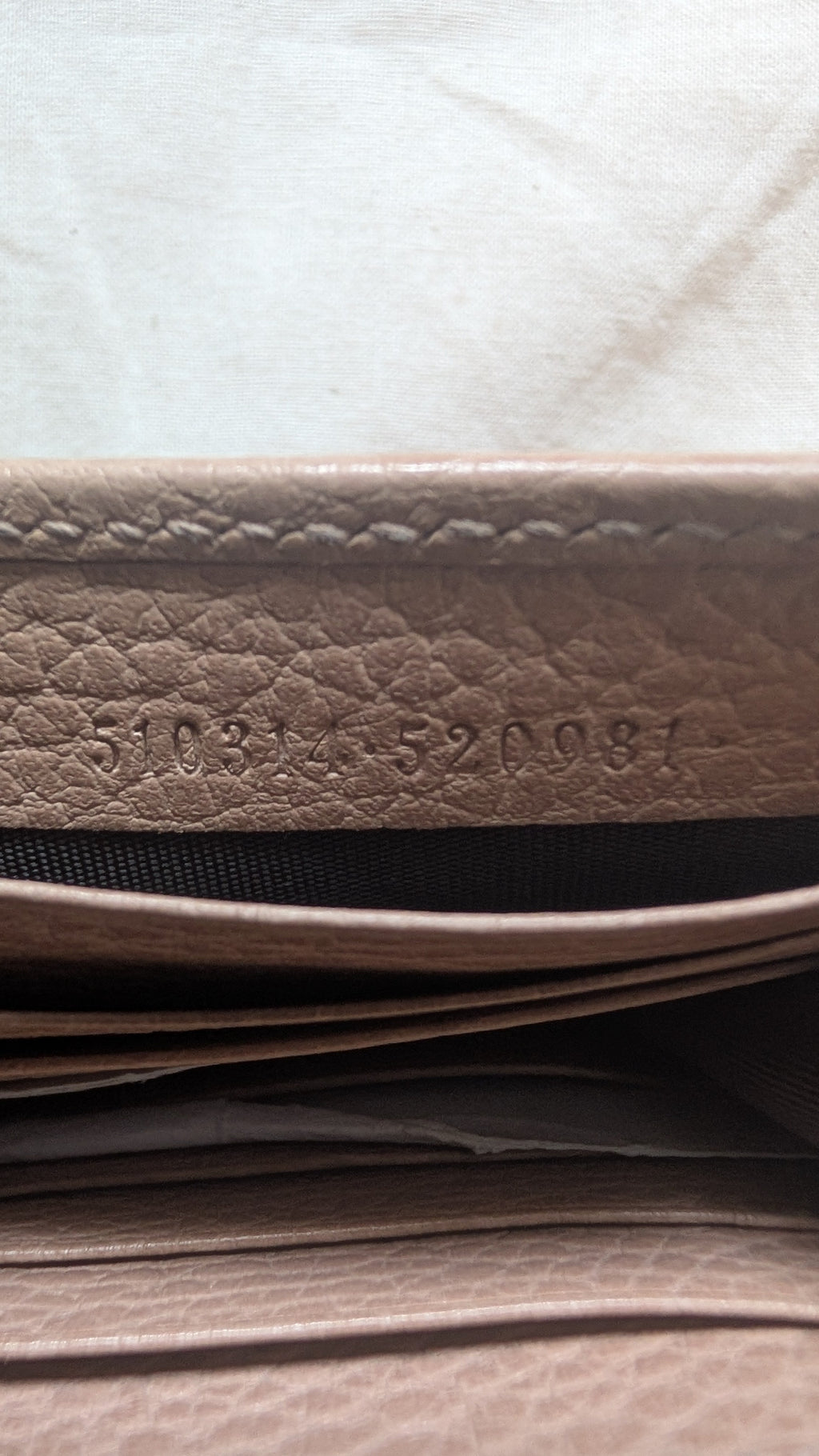 Close-up of a beige textured leather wallet showing the interior lining and stamped serial number on the leather  Pre-Owned Gucci Interlocking G Chain Wallet / Crossbody – Beige Pebbled Leatheredge.