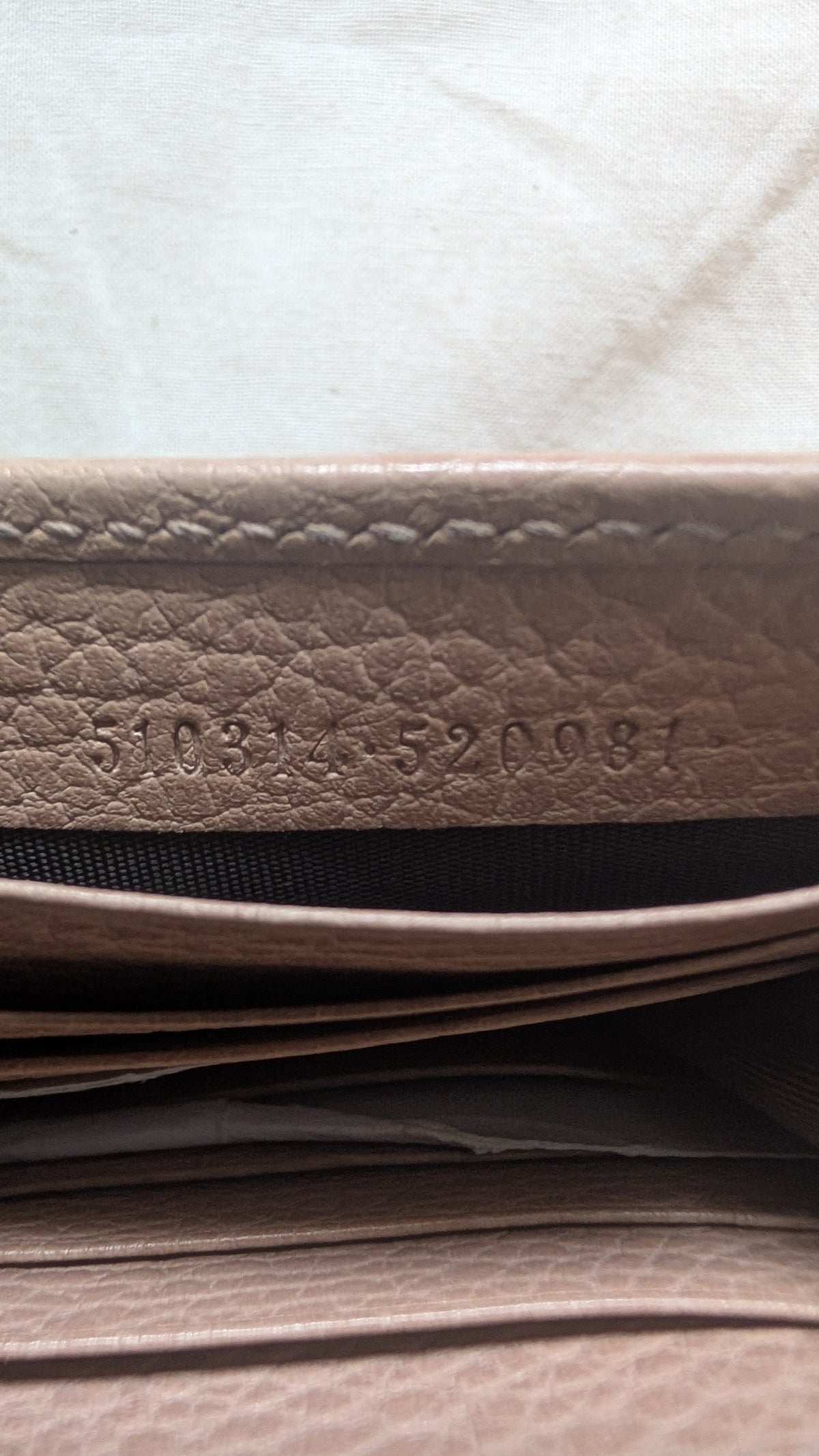 Close-up of a beige textured leather wallet showing the interior lining and stamped serial number on the leather  Pre-Owned Gucci Interlocking G Chain Wallet / Crossbody – Beige Pebbled Leatheredge.