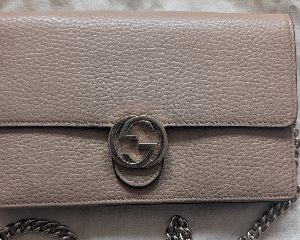 A beige pebbled leather shoulder bag with a silver-tone chain strap and a circular interlocking g logo clasp, laid flat on a textured white fabric background. Pre-Owned Gucci Interlocking G Chain Wallet / Crossbody – Beige Pebbled Leather