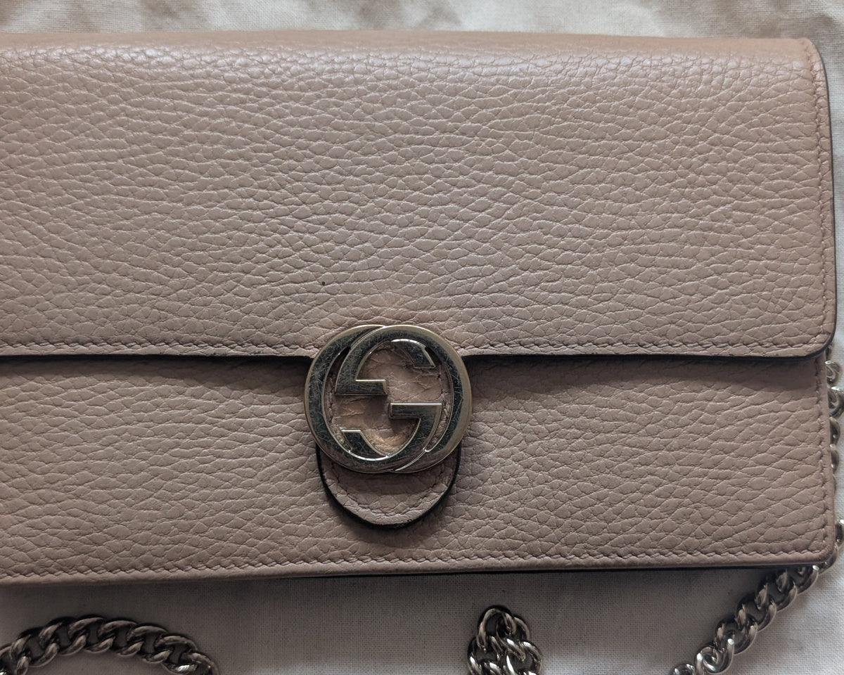 A beige pebbled leather shoulder bag with a silver-tone chain strap and a circular interlocking g logo clasp, laid flat on a textured white fabric background. Pre-Owned Gucci Interlocking G Chain Wallet / Crossbody – Beige Pebbled Leather