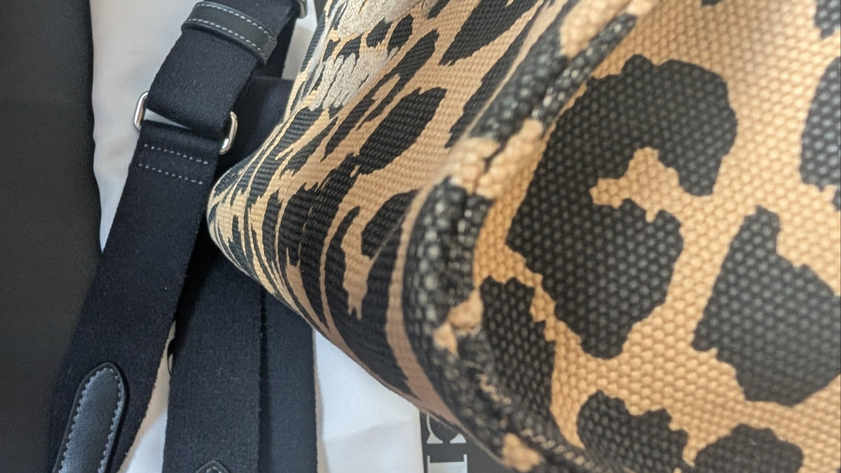 Close-up of a leopard-print fabric bag or accessory with a black strap, shown against a white fabric background. Pre-Owned Coach Cargo Tote  Leopard Print Canvas Bag
