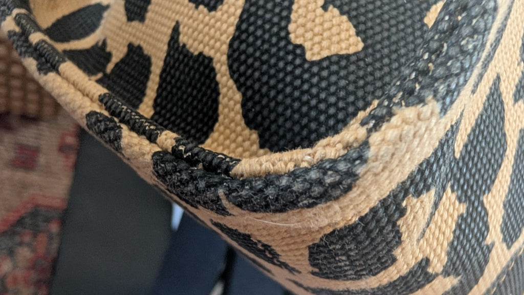 Close-up of a woven textile with a beige and black leopard-style pattern, showing the texture and edge stitching. Pre-Owned Coach Cargo Tote  Leopard Print Canvas Bag