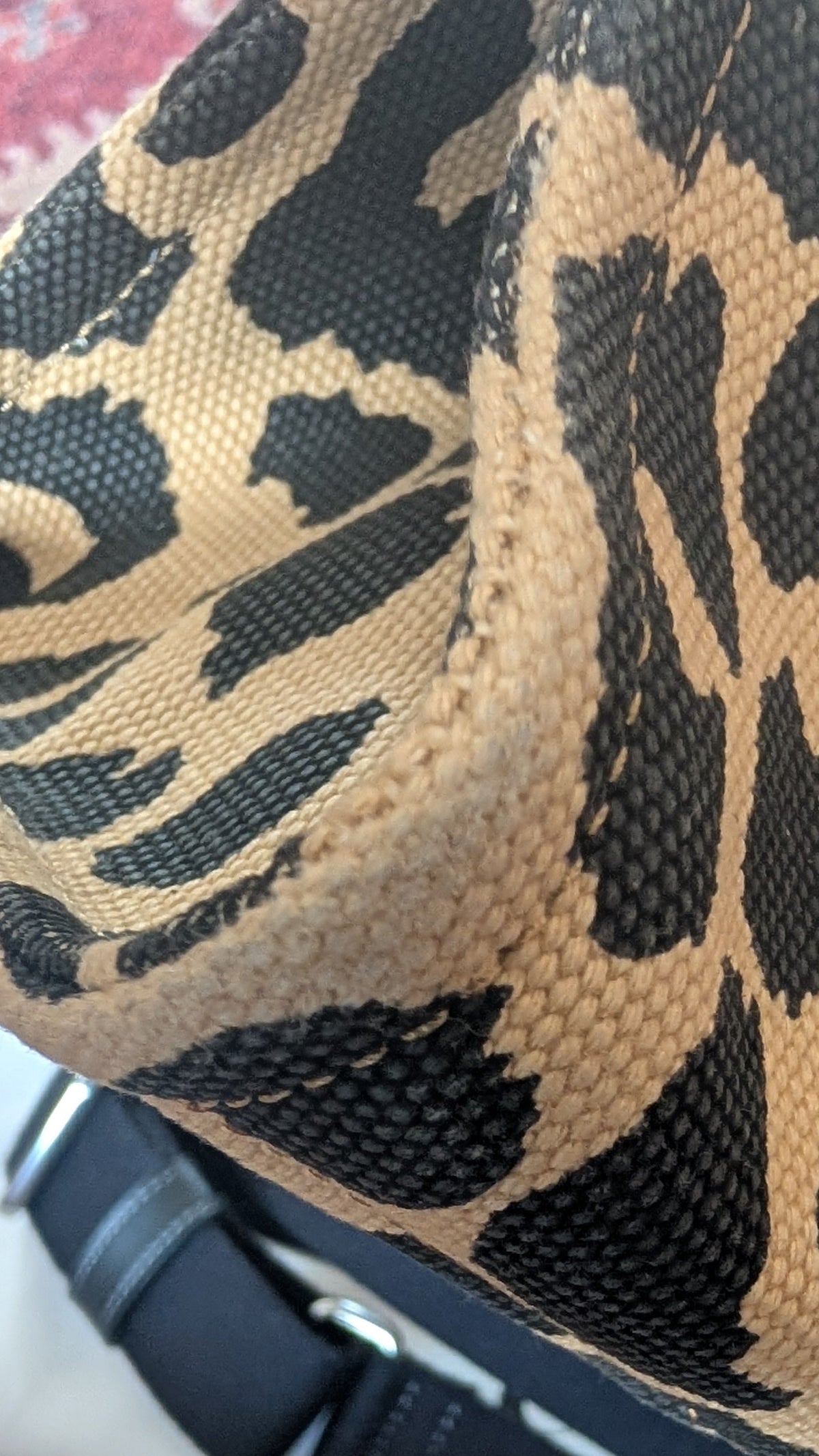 Close-up of a leopard print fabric bag with black mesh and a black strap, resting on a patterned surface. Pre-Owned Coach Cargo Tote  Leopard Print Canvas Bag