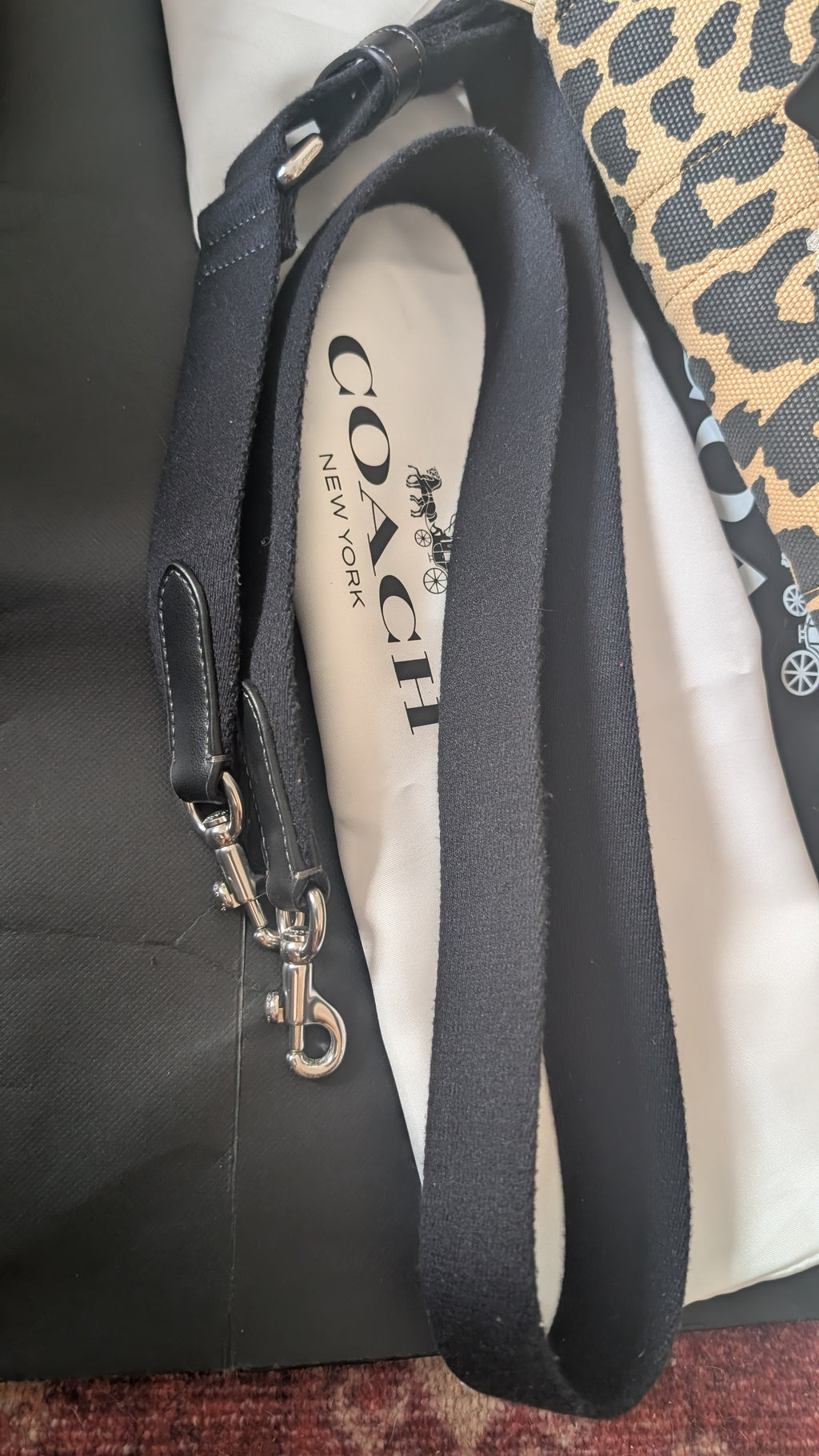A Coach shoulder strap with silver-tone hardware, laid over a white dust bag printed with the Coach logo, next to a black bag and a leopard print fabric. Pre-Owned Coach Cargo Tote  Leopard Print Canvas Bag
