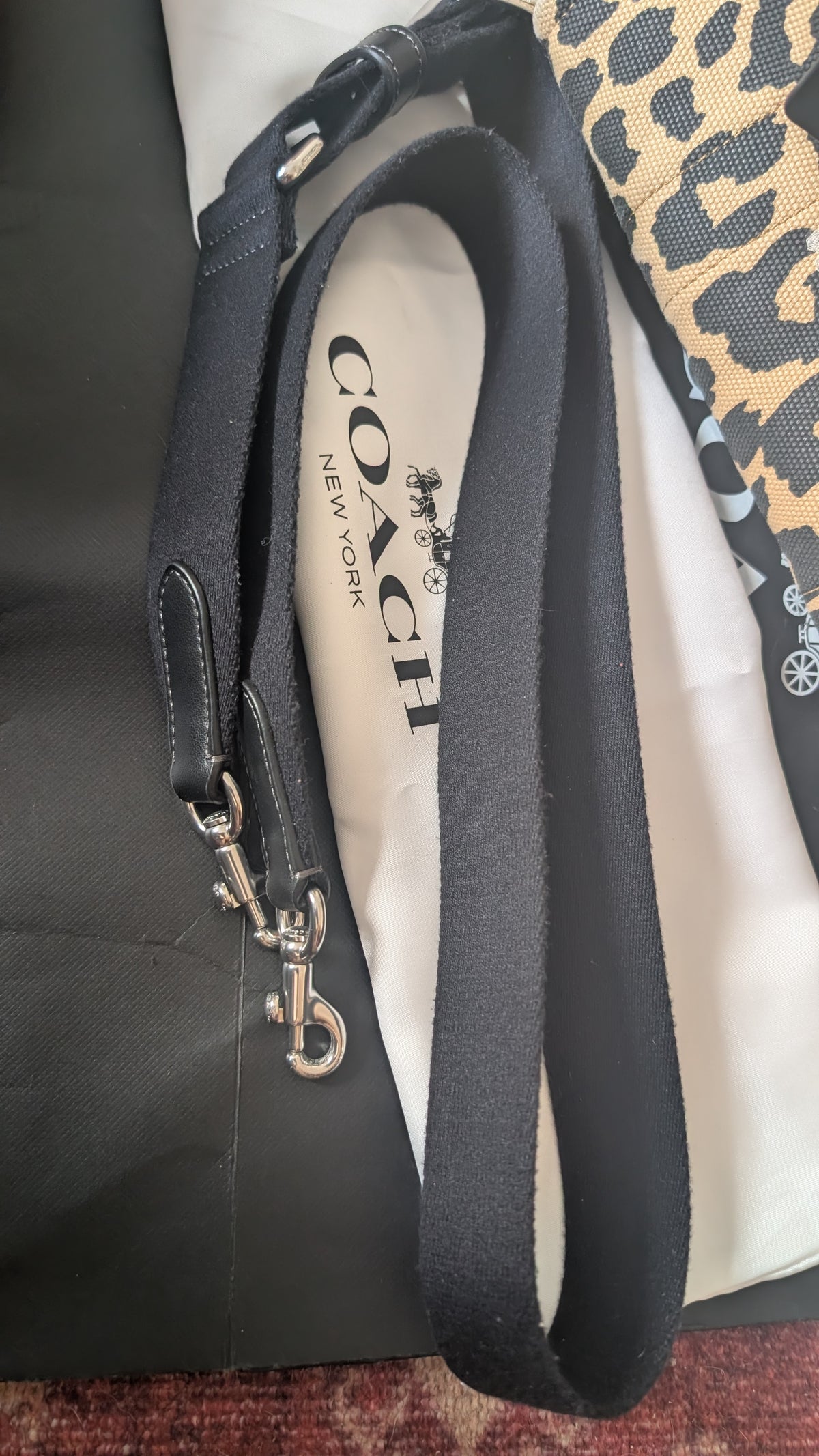 A Coach shoulder strap with silver-tone hardware, laid over a white dust bag printed with the Coach logo, next to a black bag and a leopard print fabric. Pre-Owned Coach Cargo Tote  Leopard Print Canvas Bag