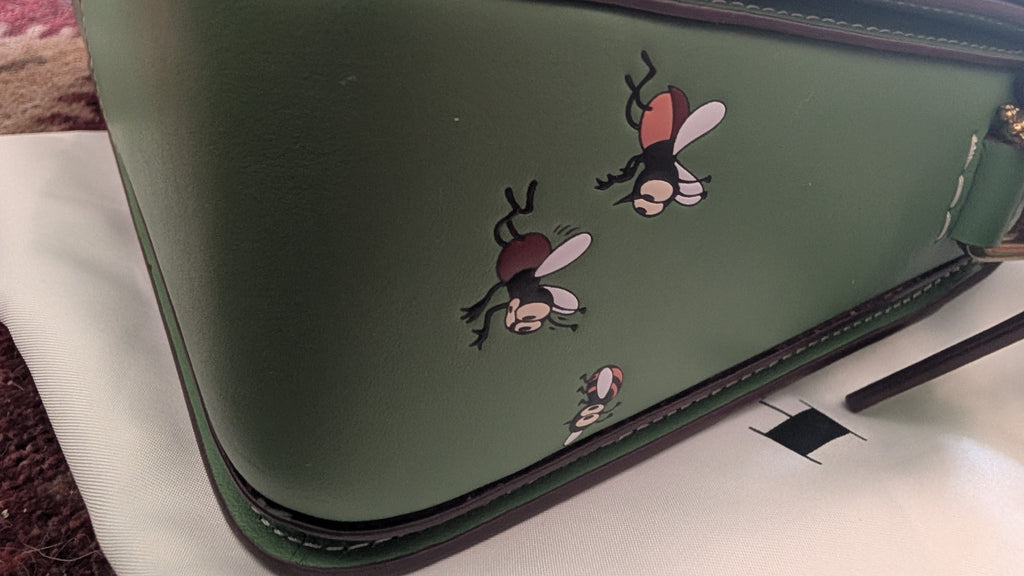 A close-up of  green leather handbag featuring hand-painted cartoon flies on the side, resting on a white surface. Pre-Owned Coach x Disney Tabby Shoulder Bag – Mickey Mouse – Green – Limited Edition
