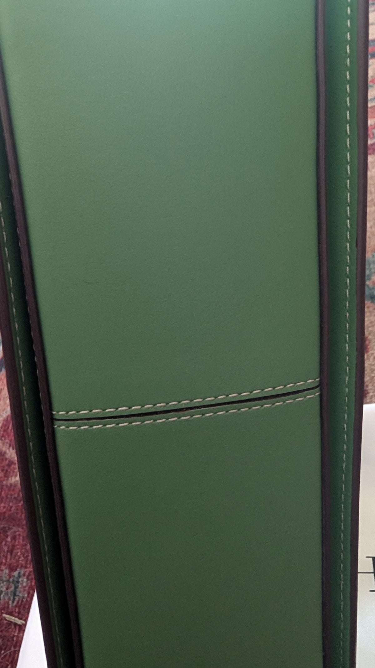A close-up of a green leather or faux-leather panel with visible stitching, likely part of a chair or upholstered furniture piece. Pre-Owned Coach x Disney Tabby Shoulder Bag – Mickey Mouse – Green – Limited Edition