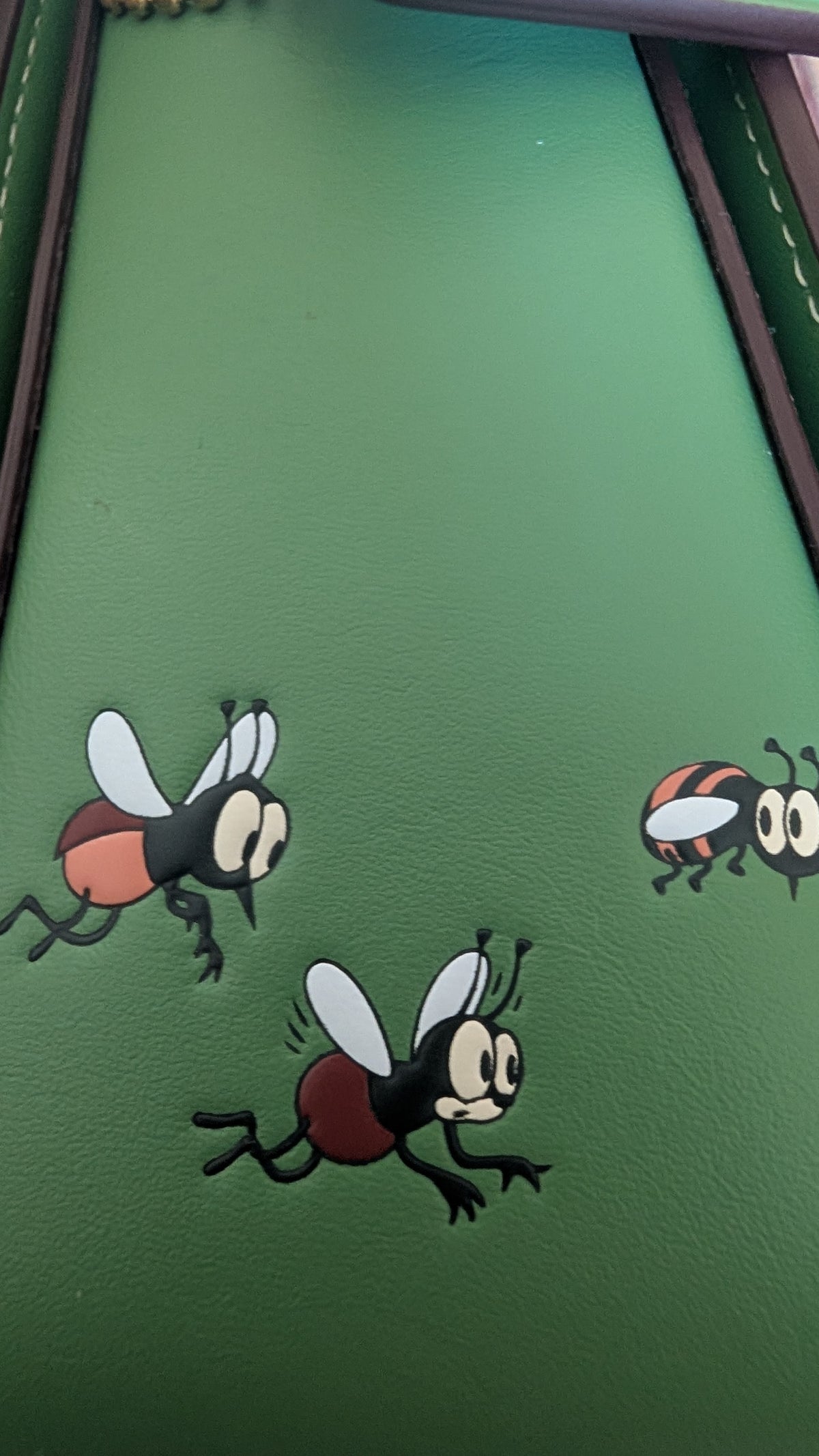 A close-up of a green hanbagsurface featuring cartoon fly graphics printed on it. Pre-Owned Coach x Disney Tabby Shoulder Bag – Mickey Mouse – Green – Limited Edition