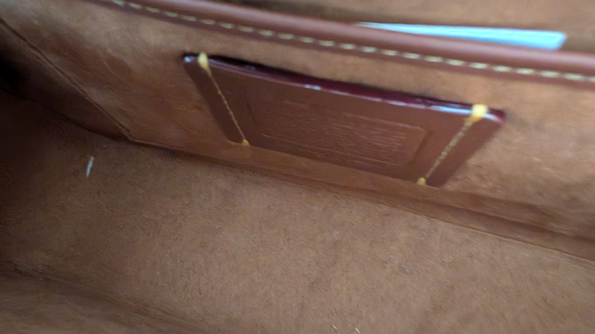 Close-up of a brown leather interior pocket with white contrast stitching and a small dark brown label attached by yellow string. Pre-Owned Coach x Disney Tabby Shoulder Bag – Mickey Mouse – Green – Limited Edition