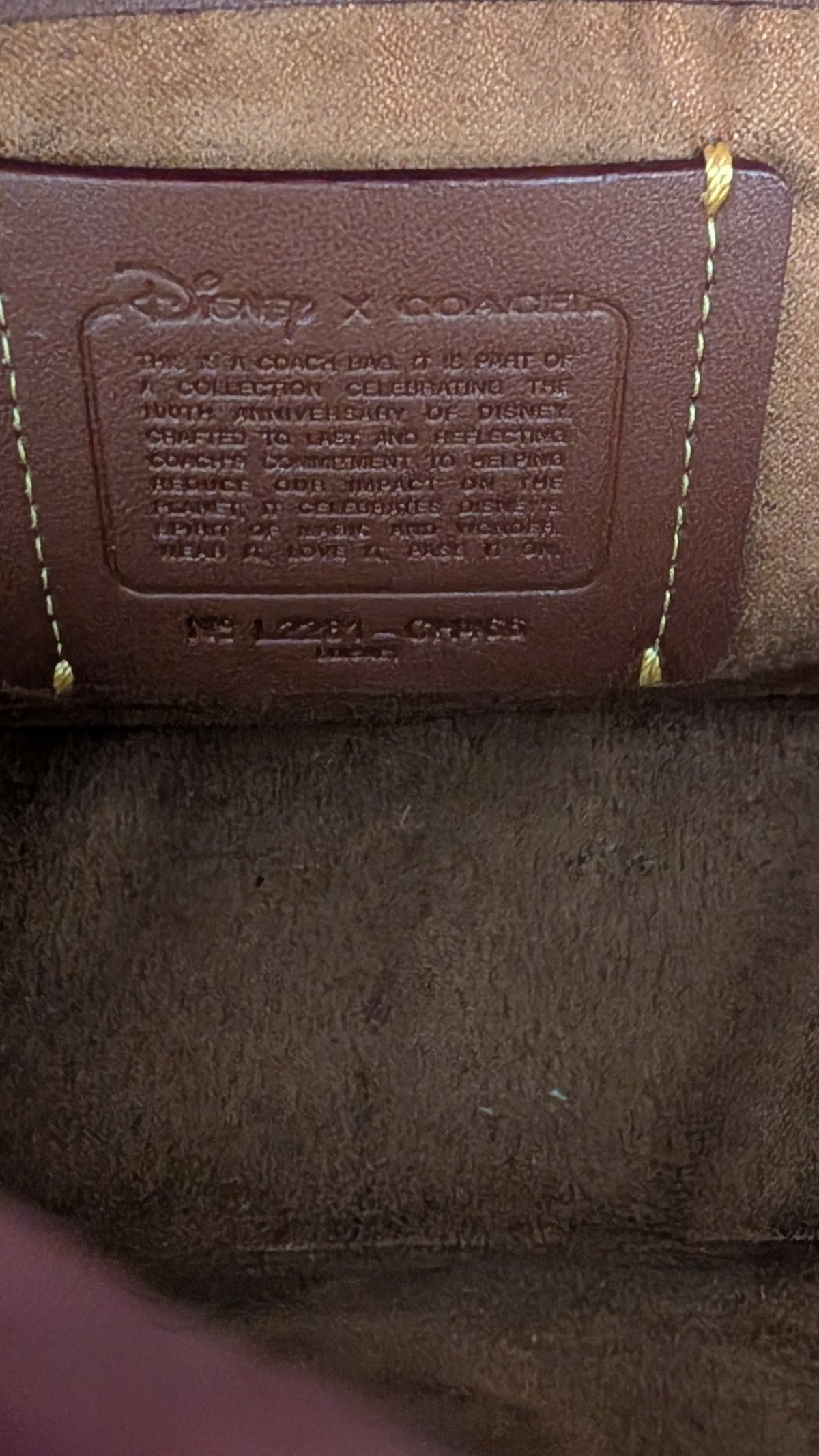 Close-up of a brown leather and canvas shoulder bag interior showing a Disney x Coach label patch and a hand pointing at the top edge. Pre-Owned Coach x Disney Tabby Shoulder Bag – Mickey Mouse – Green – Limited Edition