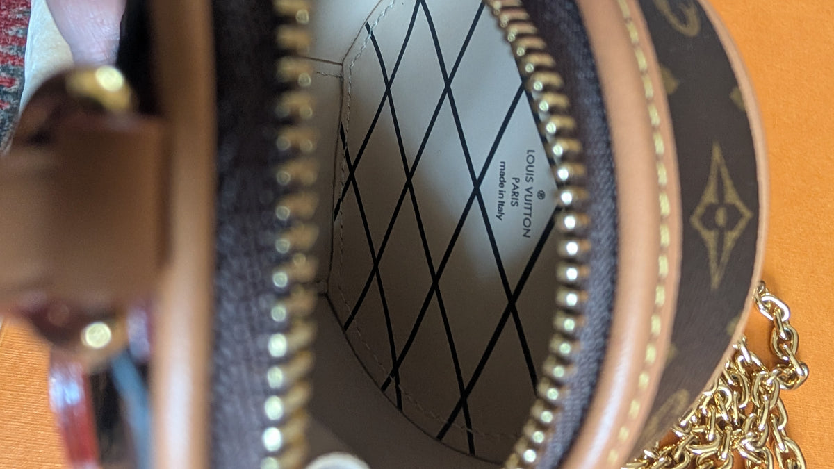Close-up of the interior of a Louis Vuitton monogram handbag, showing the white quilted lining with black diamond pattern and the brand name printed inside, framed by brown leather and gold-tone hardware. Pre-Owned Louis Vuitton Monogram Mini Boîte Chapeau Crossbody Bag – Full Set