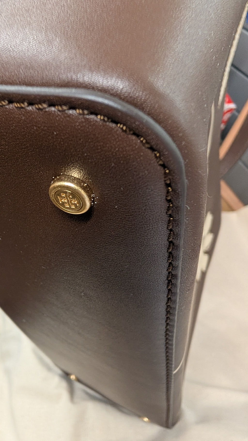 Close-up of a dark brown leather bag corner showing a gold-tone metal snap button and whipstitched edges. Pre-Owned Tory Burch  Floral Applique Top Handle Bag