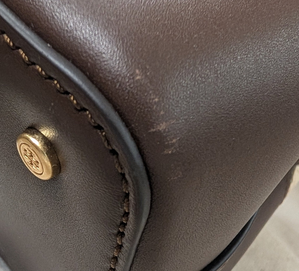 Close-up of a dark brown leather handbag corner showing gold-tone hardware, stitching, and a dust bag underneath. Pre-Owned Tory Burch  Floral Applique Top Handle Bag