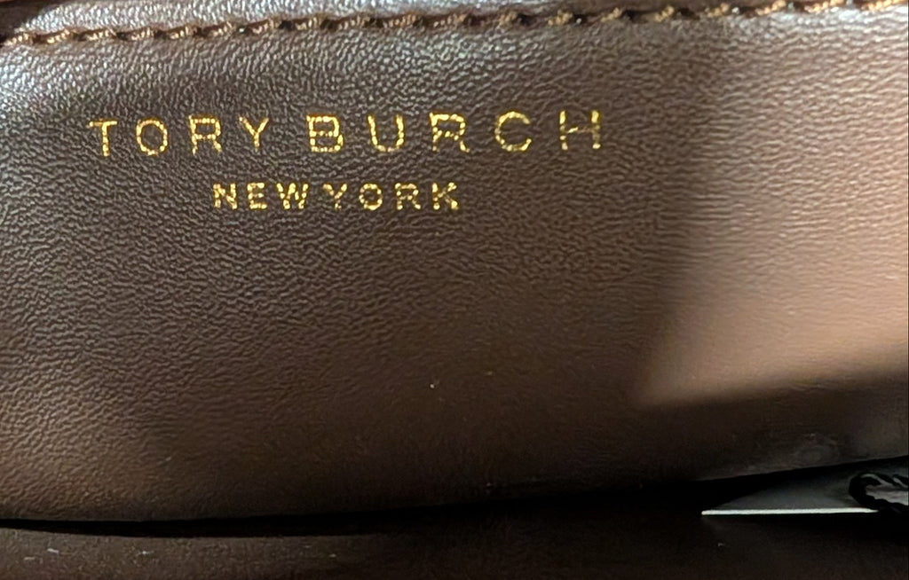 Close-up of a brown leather interior of a handbag with gold-embossed 'TORY BURCH NEW YORK' text and a hand holding the flap open. Pre-Owned Tory Burch  Floral Applique Top Handle Bag
