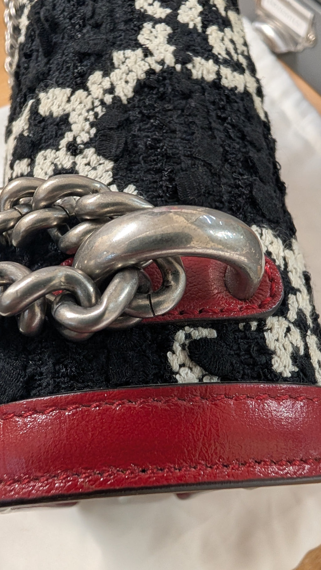 Close-up of a handbag featuring a black and white textured woven pattern, a chunky silver chain strap, and a red leather trim. Pre-Owned Gucci Dionysus GG Tweed Medium Shoulder Bag – Red/Black
