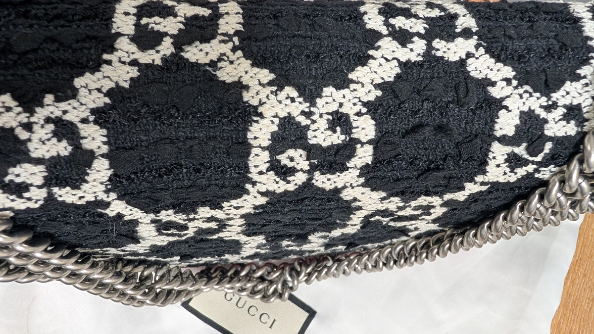 Close-up of a Gucci shoulder bag featuring a black and white interlocking monogram patterned fabric and a chunky silver chain strap, with a Gucci tag visible. Pre-Owned Gucci Dionysus GG Tweed Medium Shoulder Bag – Red/Black
