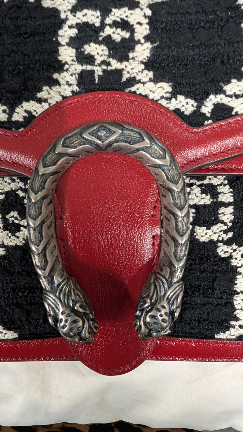 Close-up of a red leather strap and buckle closure with a silver-toned decorative horsebit-style hardware, set against a black and white patterned textile background. Pre-Owned Gucci Dionysus GG Tweed Medium Shoulder Bag – Red/Black