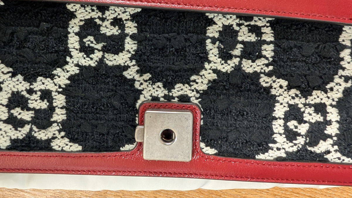 Close-up of a Gucci handbag featuring the brand's interlocking GG monogram pattern in black and off-white on a textured fabric panel, framed by red leather trim and a silver-tone metal clasp. Pre-Owned Gucci Dionysus GG Tweed Medium Shoulder Bag – Red/Black