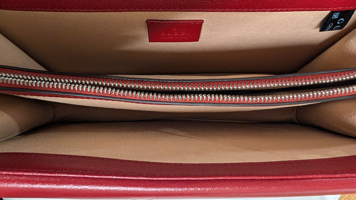 Close-up interior view of a red leather clutch or wallet showing the tan fabric lining, a horizontal silver zipper, and a small red interior label. Pre-Owned Gucci Dionysus GG Tweed Medium Shoulder Bag – Red/Black