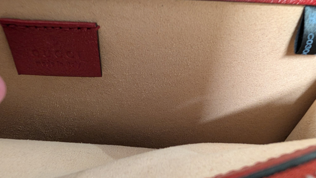 Close-up of the interior of a beige textured handbag, showing a red leather patch with debossed branding and a blue fabric tag on the right side. Pre-Owned Gucci Dionysus GG Tweed Medium Shoulder Bag – Red/Black