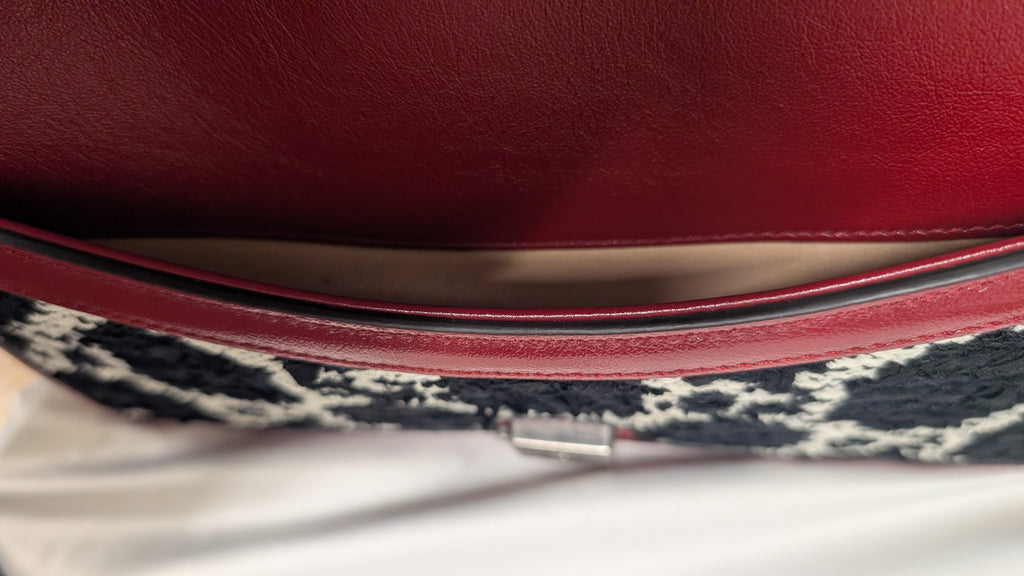 Close-up of a handbag showing a deep red leather interior lining, a thin dark trim, and a black-and-white patterned fabric exterior. Pre-Owned Gucci Dionysus GG Tweed Medium Shoulder Bag – Red/Black