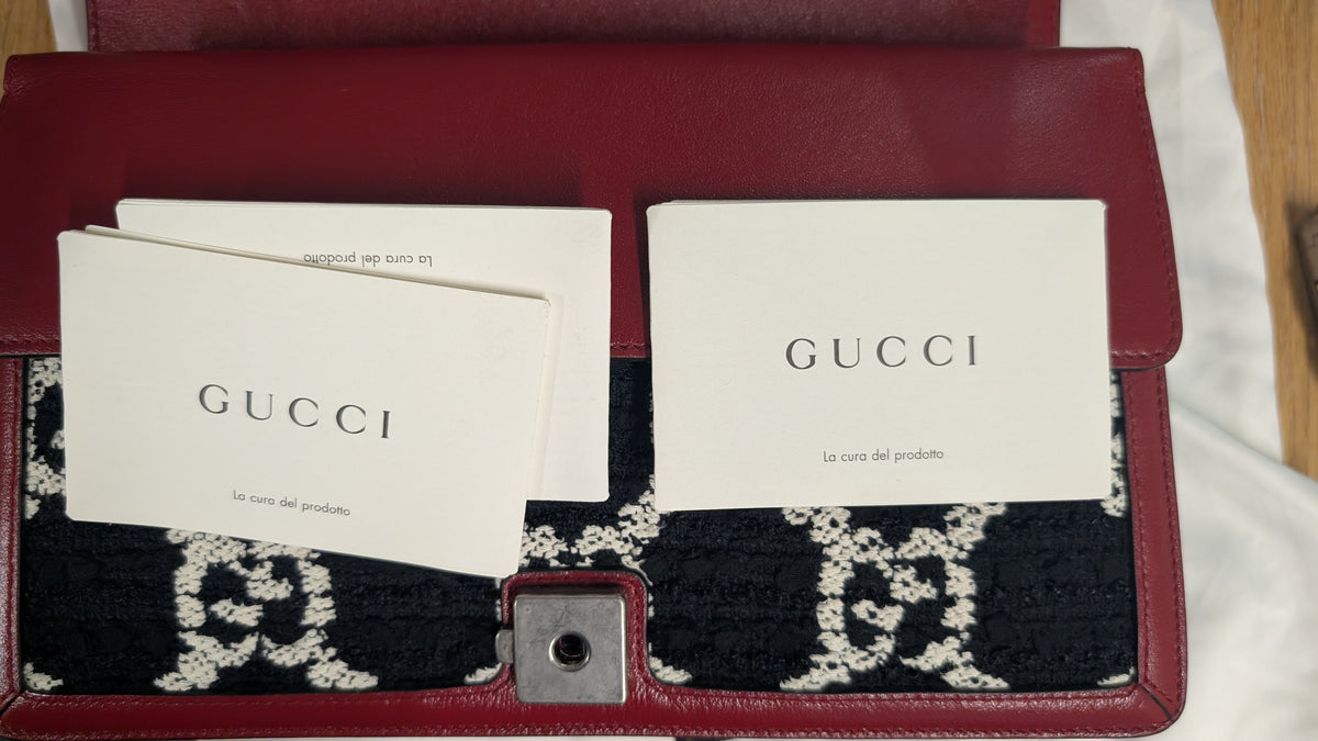 A red leather Gucci clutch or wallet shown open, with white Gucci paper cards and a black-and-white patterned fabric insert visible inside. The Gucci wordmark is printed on the cards. Pre-Owned Gucci Dionysus GG Tweed Medium Shoulder Bag – Red/Black