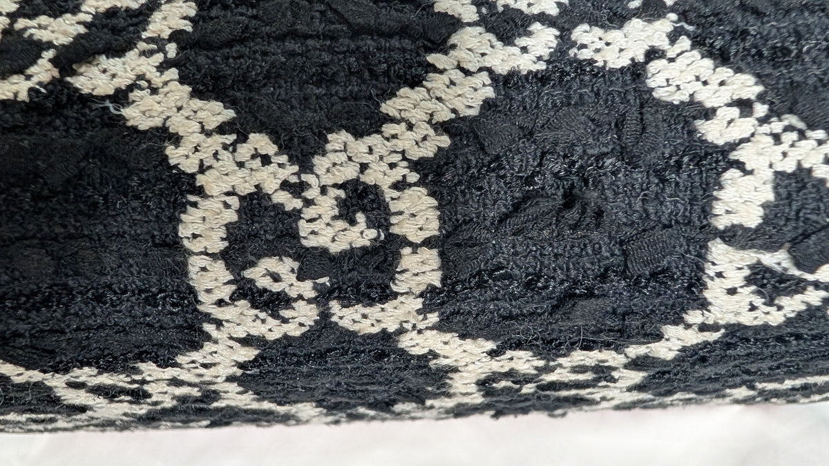 A close-up of a textured black and off-white woven fabric with a repeating geometric pattern. 