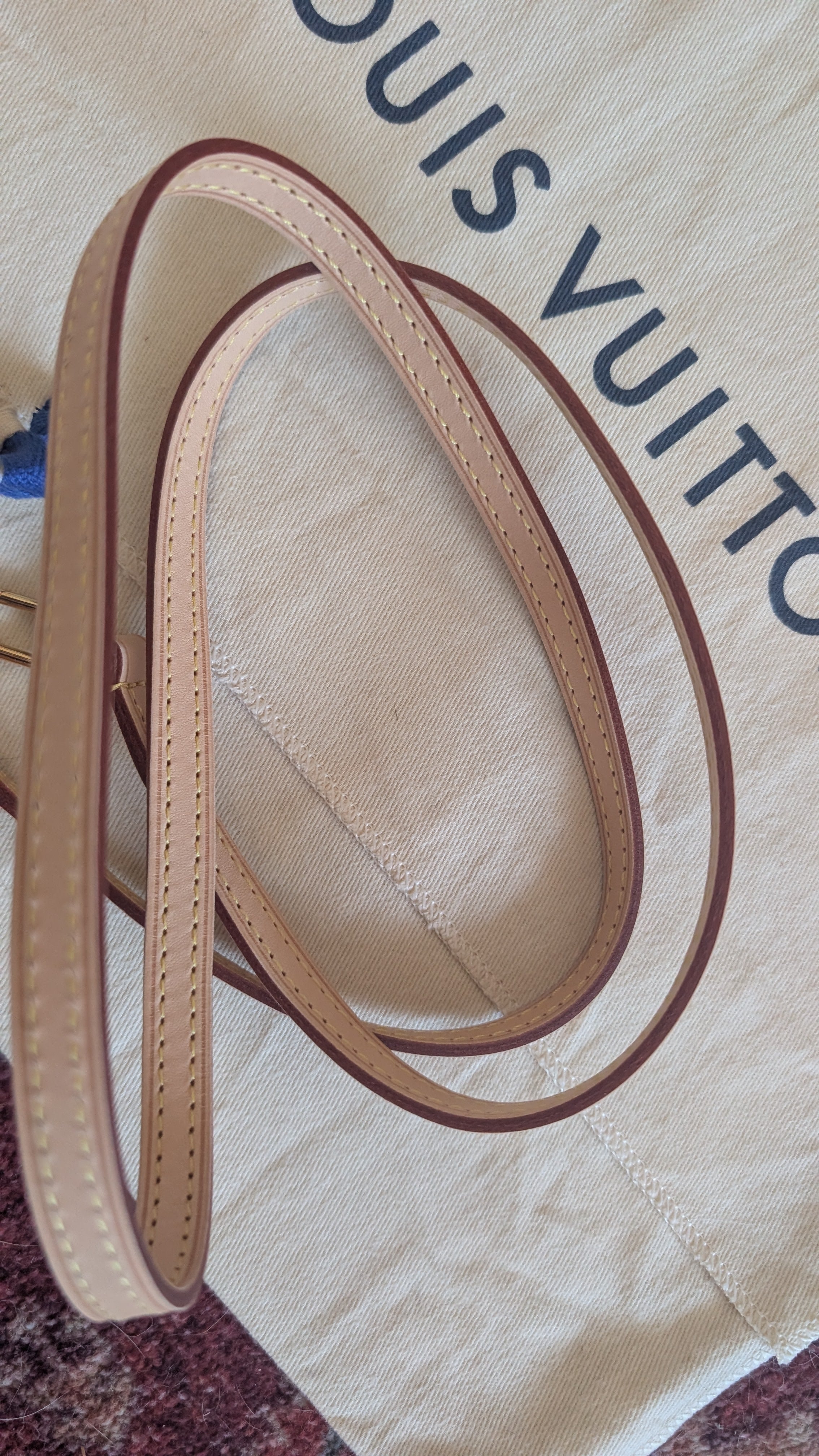 A beige leather strap with dark brown edging and stitching, coiled on a cream-colored Louis Vuitton dust bag. Pre-Owned Louis Vuitton Alma BB Monogram World Tour / Travel Sticker Shoulder Bag