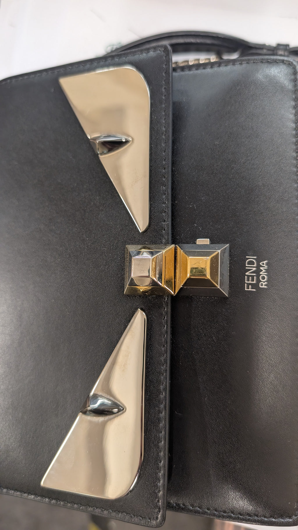 Close-up of a black leather Fendi Marmont handbag featuring the signature metallic gold and silver chevron hardware and the 'FENDI MARMONT' branding on the front flap. Pre-Owned Fendi Kan I Monster Eyes Black Leather Chain Shoulder Bag