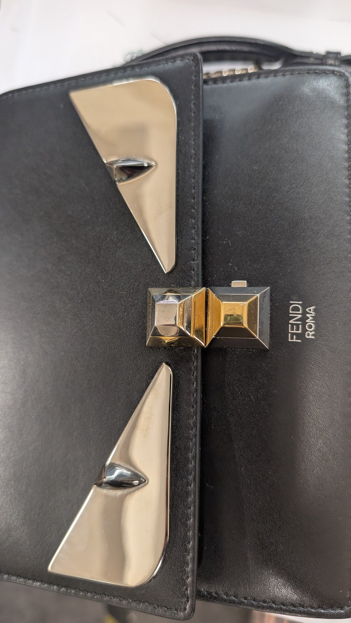 Close-up of a black leather Fendi Marmont handbag featuring the signature metallic gold and silver chevron hardware and the 'FENDI MARMONT' branding on the front flap. Pre-Owned Fendi Kan I Monster Eyes Black Leather Chain Shoulder Bag