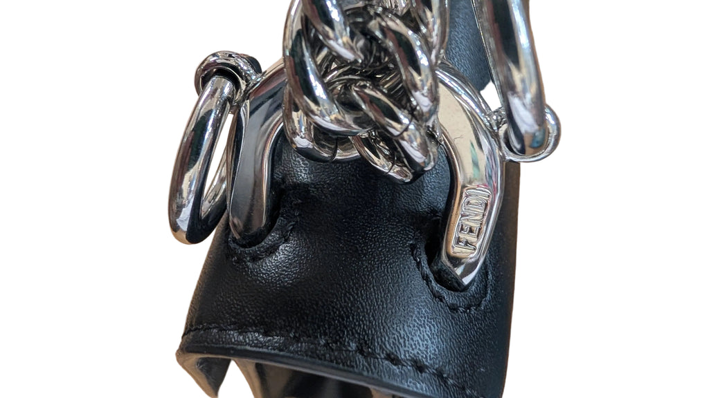 Close-up of a black leather handbag featuring a chunky silver chain strap and a silver metal D-ring closure, resting on a wooden surface. Pre-Owned Fendi Kan I Monster Eyes Black Leather Chain Shoulder Bag