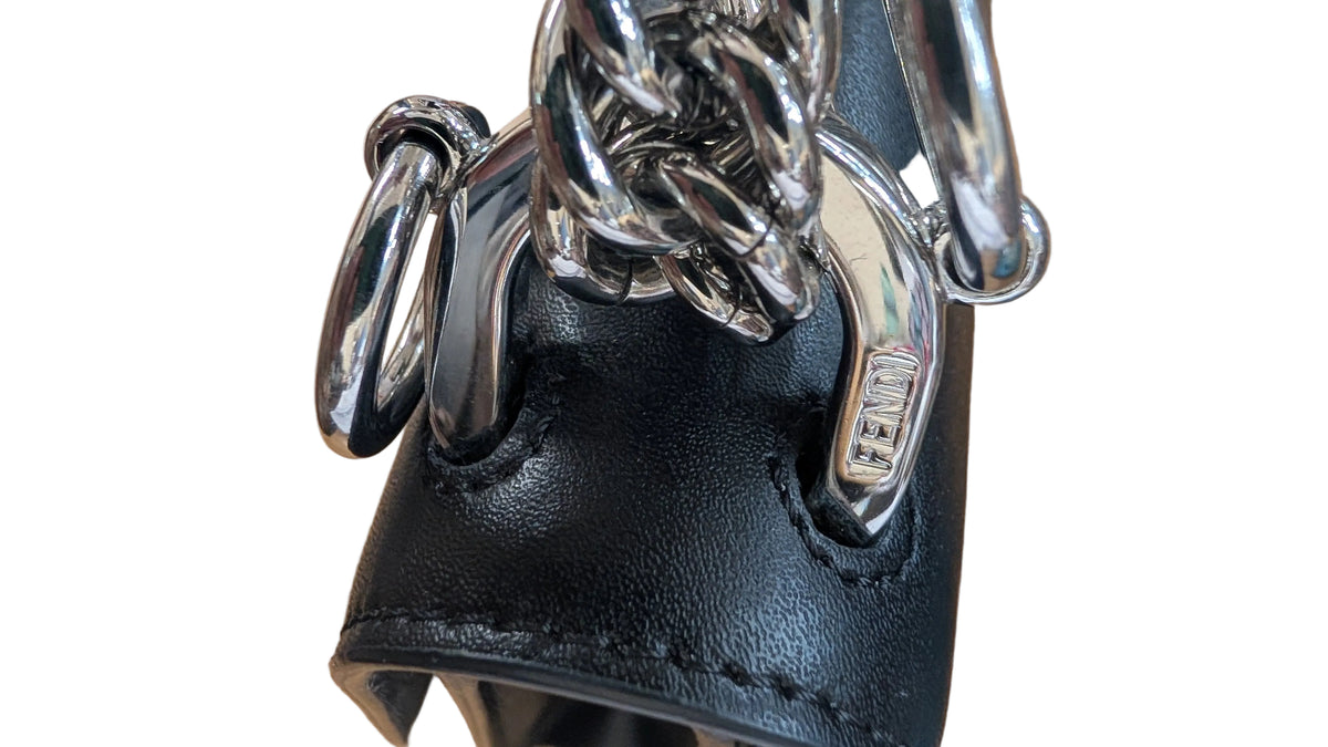 Close-up of a black leather handbag featuring a chunky silver chain strap and a silver metal D-ring closure, resting on a wooden surface. Pre-Owned Fendi Kan I Monster Eyes Black Leather Chain Shoulder Bag