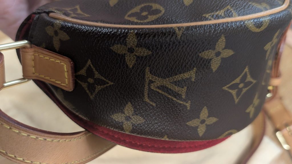 A close-up of a Louis Vuitton monogram canvas pouch with a tan leather strap and gold-tone hardware, resting on a light wooden surface. Pre-Owned Louis Vuitton Monogram Tambourin Shoulder / Crossbody Bag