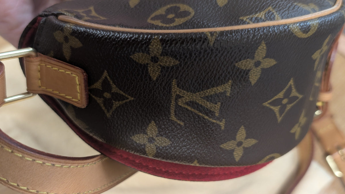 A close-up of a Louis Vuitton monogram canvas pouch with a tan leather strap and gold-tone hardware, resting on a light wooden surface. Pre-Owned Louis Vuitton Monogram Tambourin Shoulder / Crossbody Bag