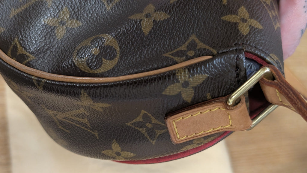 A close-up of a Louis Vuitton monogram canvas shoulder bag in dark brown with tan leather trim and strap, resting on a light wood surface. Pre-Owned Louis Vuitton Monogram Tambourin Shoulder / Crossbody Bag