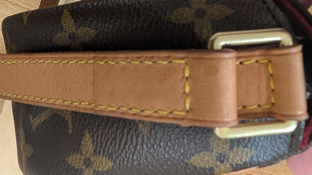 Close-up of a Louis Vuitton monogram shoulder bag with a tan leather strap and gold-tone buckle, held by a hand over a light wood surface. Pre-Owned Louis Vuitton Monogram Tambourin Shoulder / Crossbody Bag
