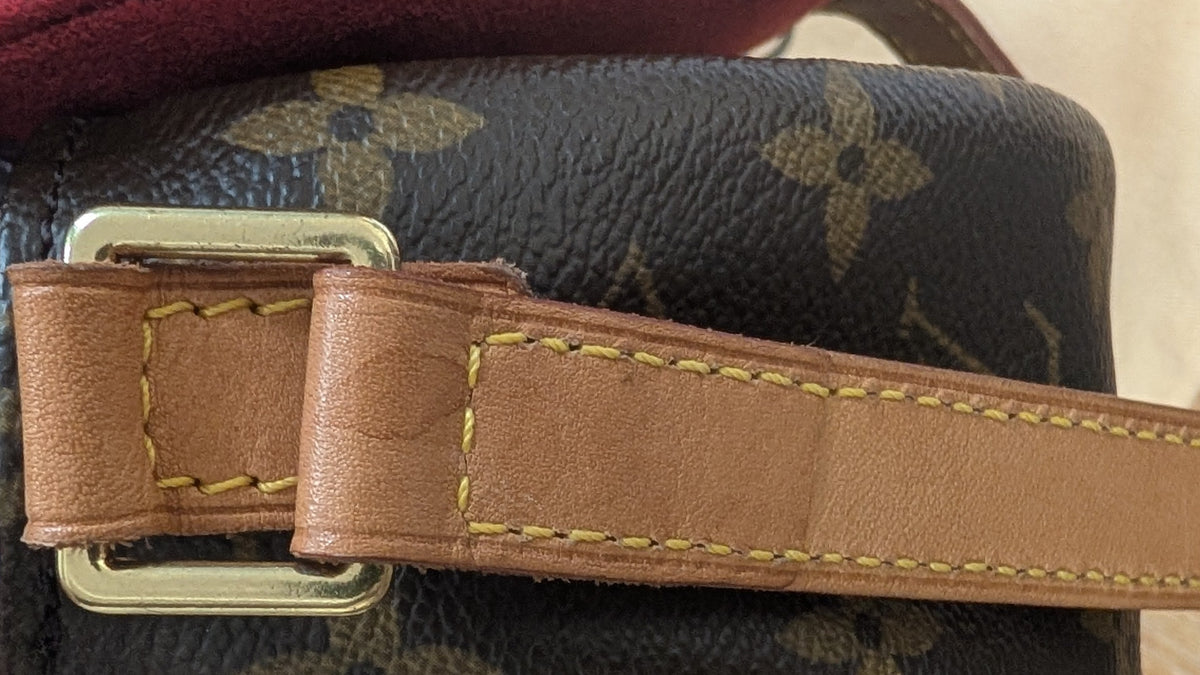 A close-up of a Louis Vuitton monogram canvas handbag with a tan leather strap and gold-tone hardware, held open by a hand over a light wood surface. Pre-Owned Louis Vuitton Monogram Tambourin Shoulder / Crossbody Bag