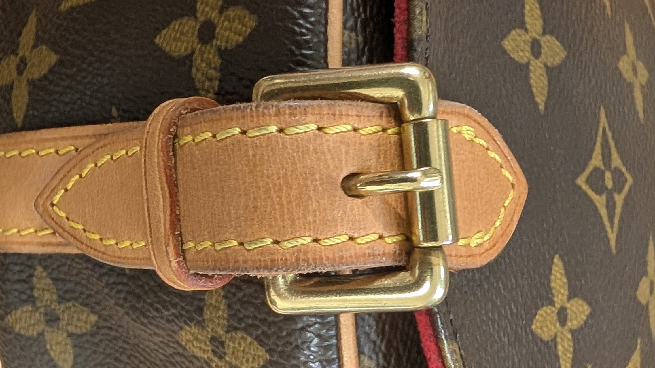 Close-up of a Louis Vuitton monogram handbag with a tan leather strap and gold-tone buckle, resting on a light wood surface. Pre-Owned Louis Vuitton Monogram Tambourin Shoulder / Crossbody Bag