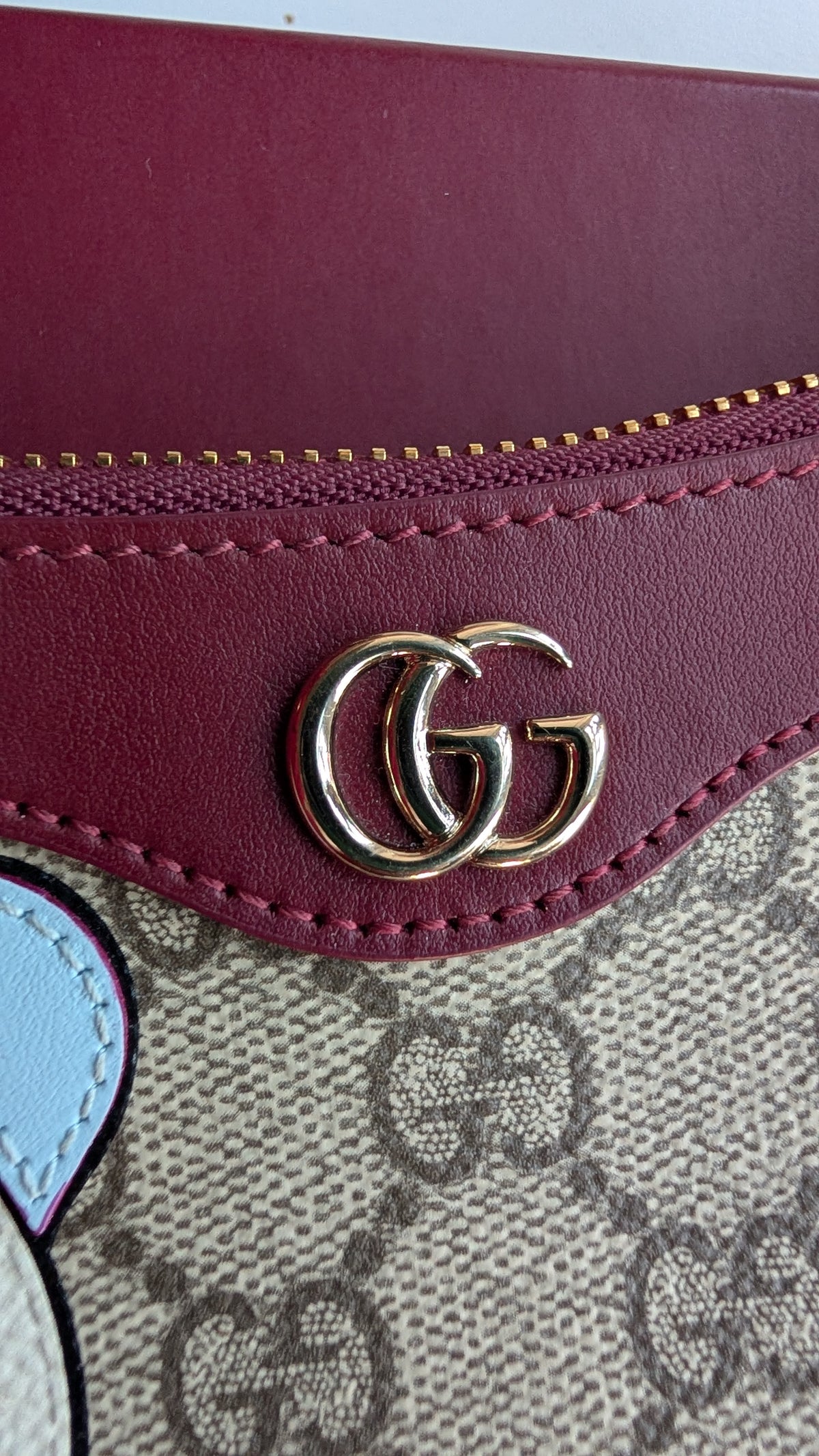 Close-up of a Gucci wallet or pouch showing a burgundy leather flap with a gold interlocking GG logo, a beige GG monogram canvas body, and a small light blue accent patch. Pre-Owned Gucci GG Supreme Ophidia Panda Mini Chain Shoulder Bag