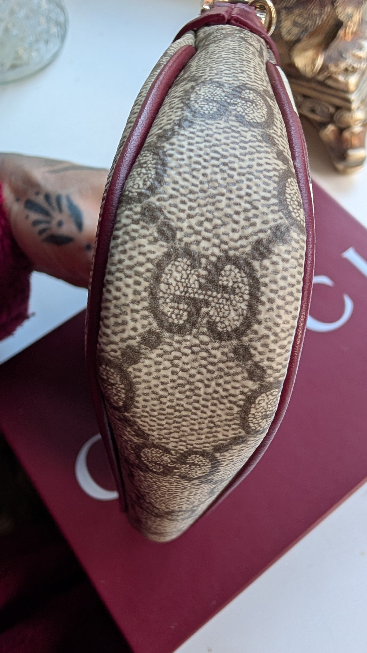 A close-up of a Gucci monogram canvas clutch or coin purse with dark red leather trim, resting on a dark red Gucci box. Pre-Owned Gucci GG Supreme Ophidia Panda Mini Chain Shoulder Bag
