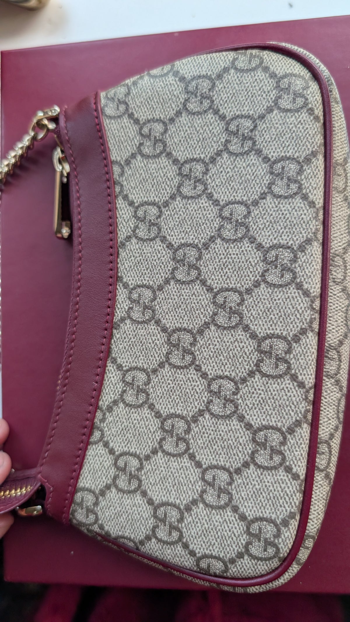 A Gucci monogram canvas wristlet bag with burgundy leather trim and a gold-tone chain strap, shown on a burgundy surface. Pre-Owned Gucci GG Supreme Ophidia Panda Mini Chain Shoulder Bag