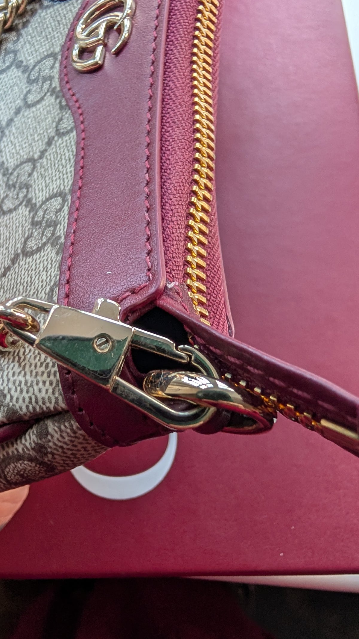 Close-up of a Gucci handbag showing the signature GG monogram canvas, burgundy leather trim, gold zipper, and metal clasp on a burgundy box. Pre-Owned Gucci GG Supreme Ophidia Panda Mini Chain Shoulder Bag