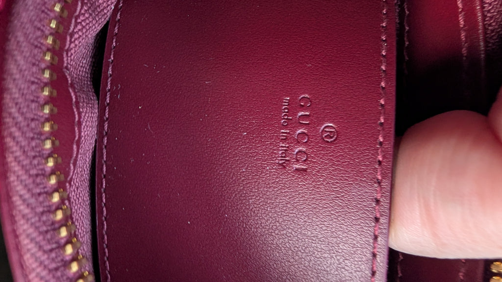 Close-up of a burgundy leather interior flap with an embossed Gucci logo and 'made in Italy' text, held by a finger next to a matching zippered pocket. Pre-Owned Gucci GG Supreme Ophidia Panda Mini Chain Shoulder Bag