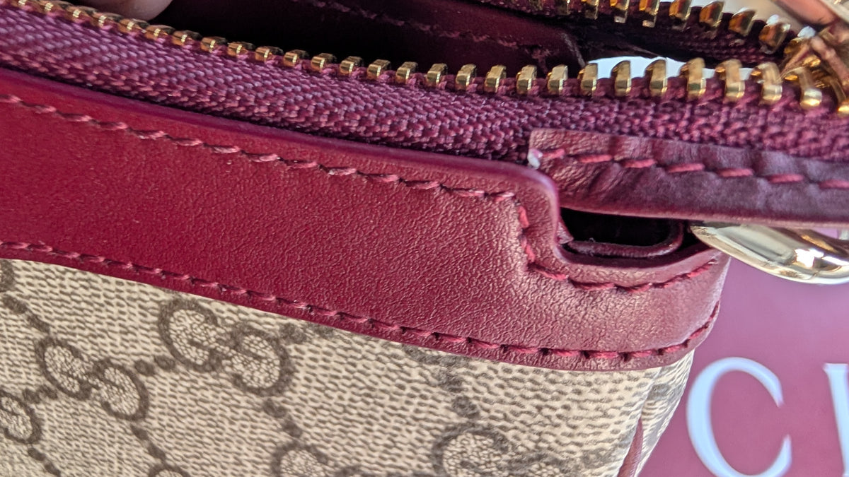 Close-up of a Gucci handbag corner showing the beige and brown GG monogram canvas, deep burgundy leather trim, gold zipper teeth, and matching stitching. Pre-Owned Gucci GG Supreme Ophidia Panda Mini Chain Shoulder Bag