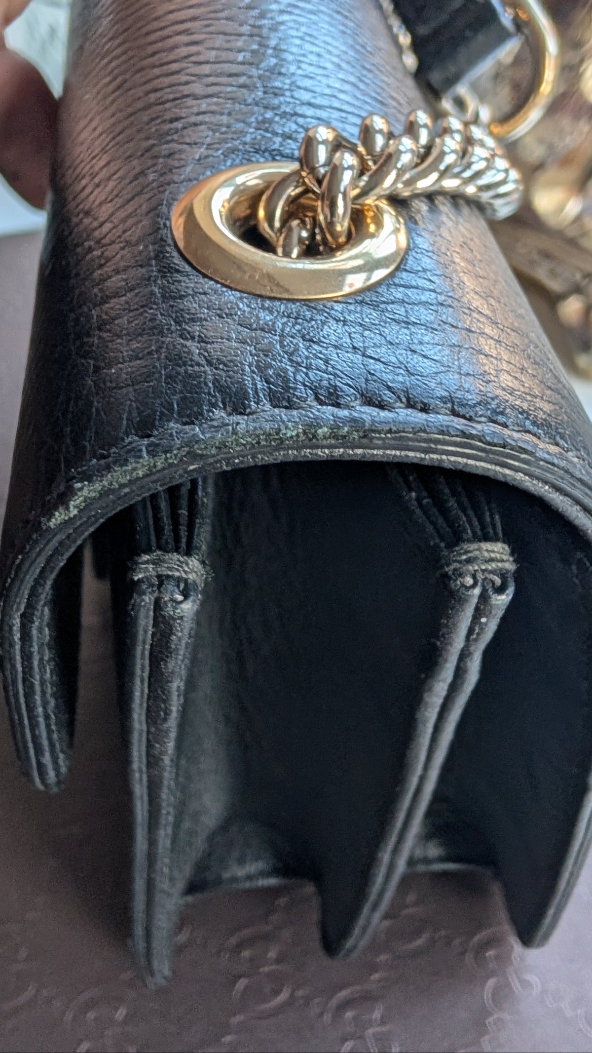 A close-up of a black textured leather handbag held by a hand, featuring a prominent gold-tone metal ring and chain strap attachment. Pre-Owned Gucci Interlocking Black shoulder bag 